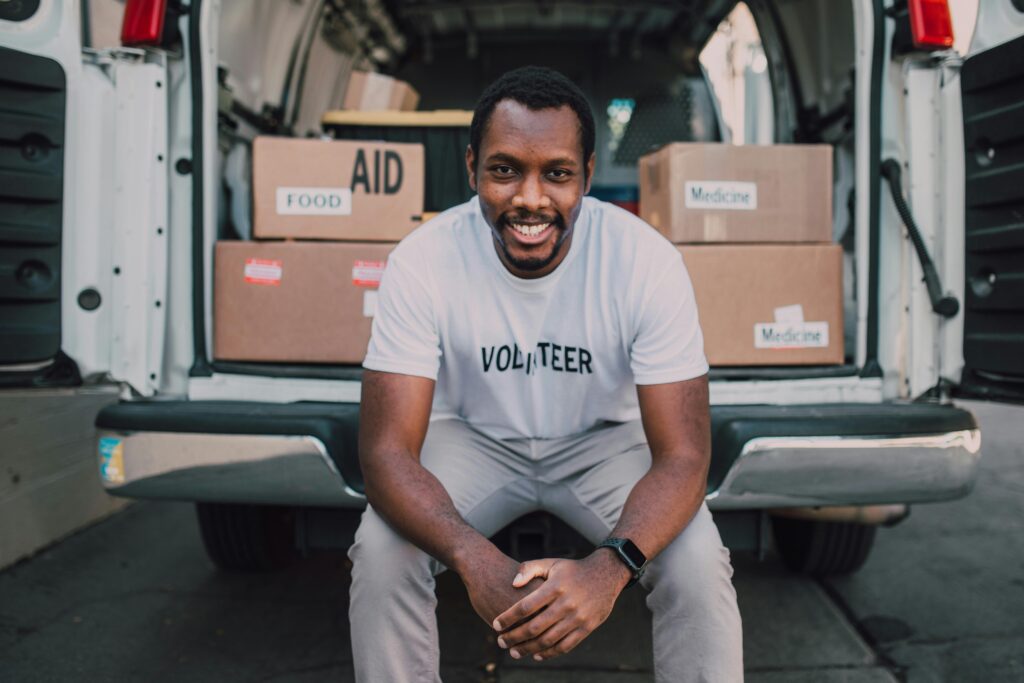 Smiling volunteer seated with boxes labeled food and medicine in a van.